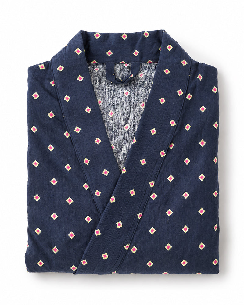 A folded navy blue robe with a repeating small pink and white diamond pattern, featuring a textured gray inner lining visible at the collar, set against a plain white background.