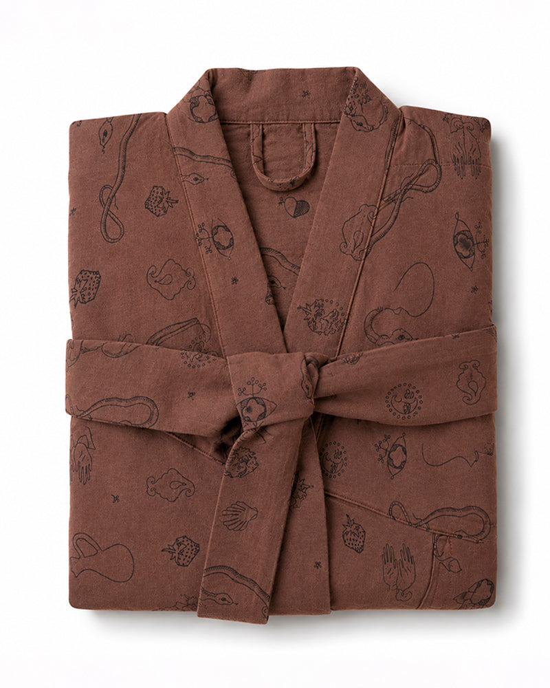 A brown cotton bathrobe with a matching tie belt, featuring a whimsical black line-art print of planets, stars, and space-themed doodles, neatly folded on a white background.