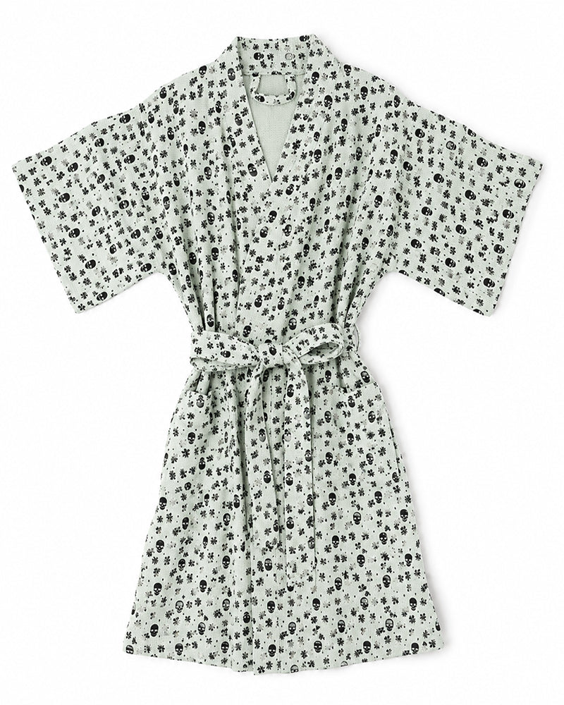 A short-sleeve robe with a tie waist, featuring an all-over black skull and crossbones print on a light background, shown flat against a white background.
